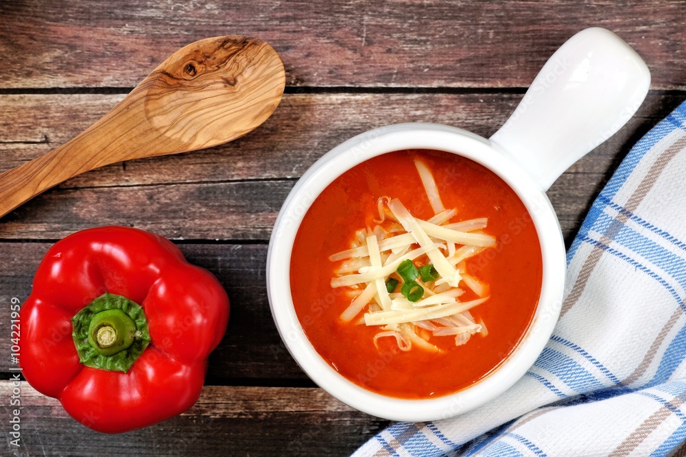 Red pepper soup topped with shredded cheese and green onions, overhead scene on rustic wood background Red pepper soup topped with shredded cheese and green onions, overhead scene on rustic wood background