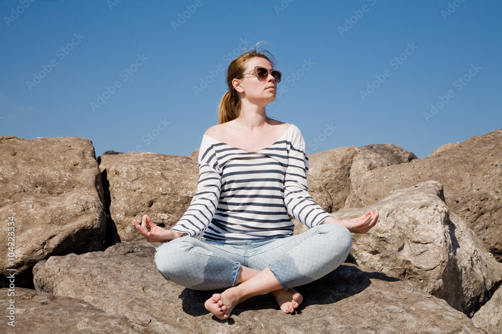 Young attractive woman meditating on the rocks against the sky