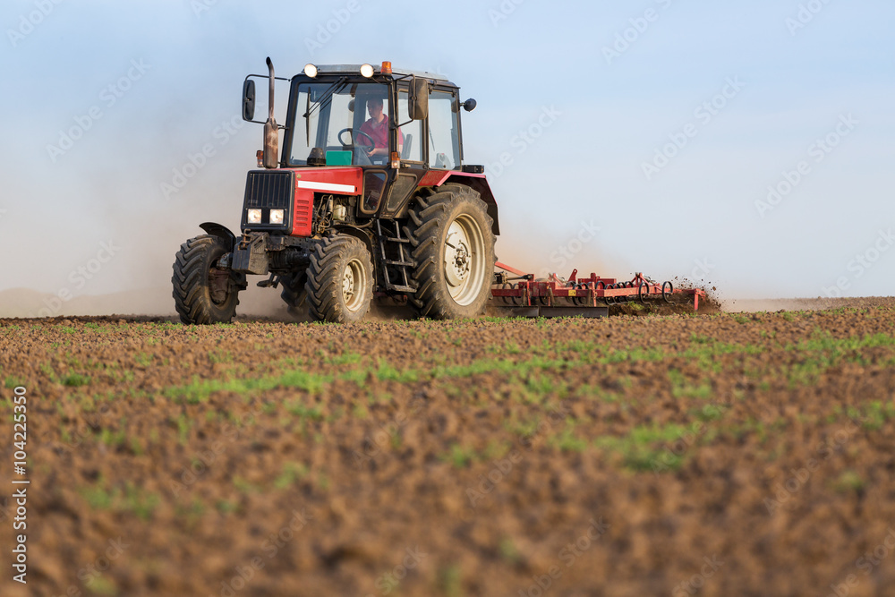 Fototapeta premium Tractor cultivating field at spring