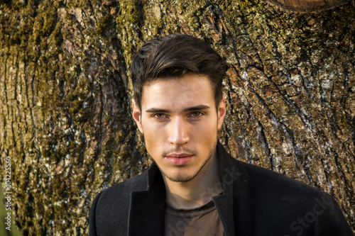 Handsome young man leaning against tree