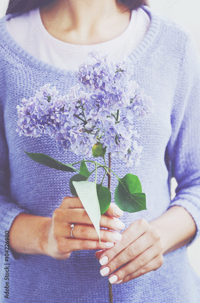 Woman in knitted sweater holding lilac flower in her hands