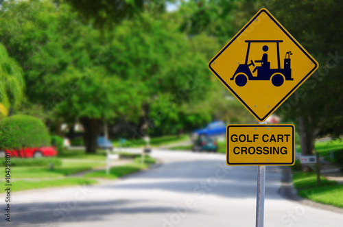 Golf Cart Crossing sign on a residential street intersection with blurred lush green trees in the background