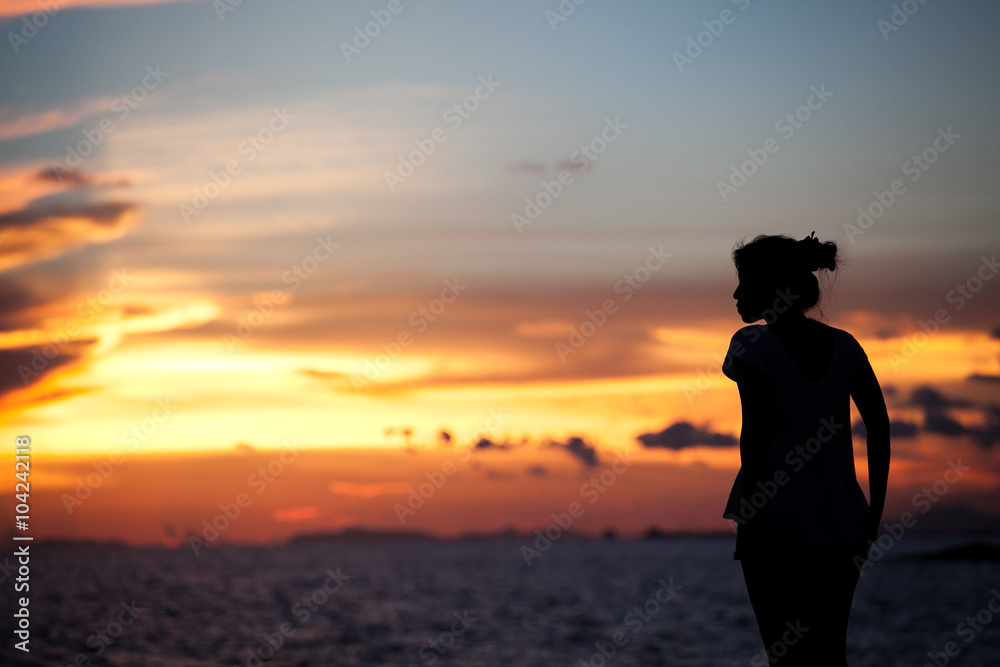 The silhouette girl on a cliff above the sea and watching the sunset