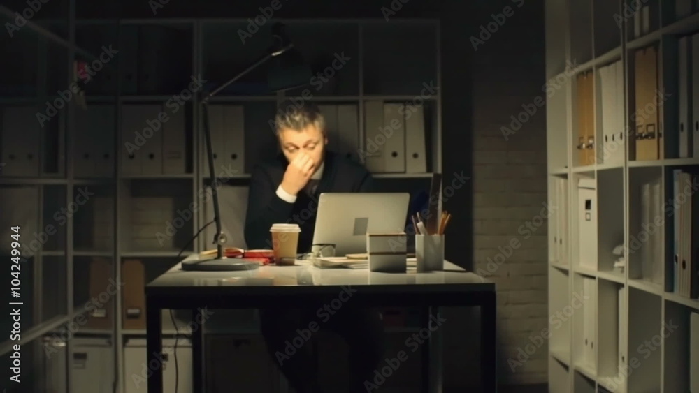 Tired office sitting in front of the laptop in dark office and covering his eyes with hands Tired office sitting in front of the laptop in dark office and covering his eyes with hands