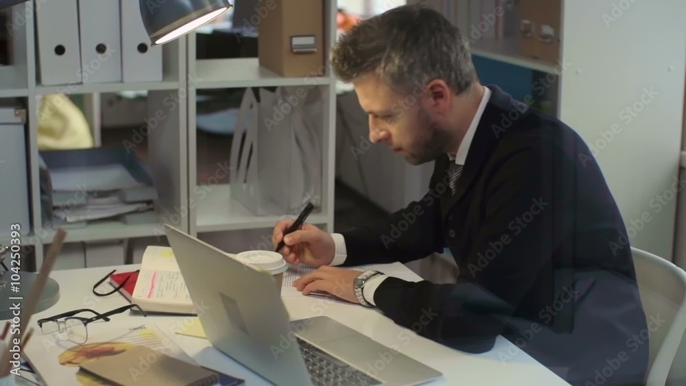 Office worker sitting at the desk, typing on laptop and working with documents Office worker sitting at the desk, typing on laptop and working with documents