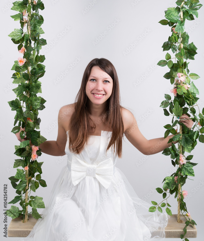 Beautiful young leggy blonde in a little white dress on a swing, wooden swing suspended from a rope hemp, rope wrapped vine and ivy Beautiful young leggy blonde in a little white dress on a swing, wooden swing suspended from a rope hemp, rope wrapped vine and ivy