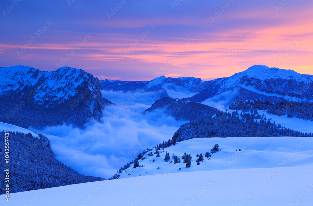 Clouds in the valley of a mountain range in French Alps during a colorful sunset.