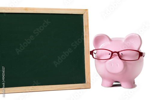 Piggy bank or piggybank wearing glasses in school or college classroom fees savings plan planning in front of small blank blackboard isolated on white background space for copy text photo