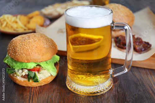Glass mug of light beer with hamburgers on dark wooden table, close up