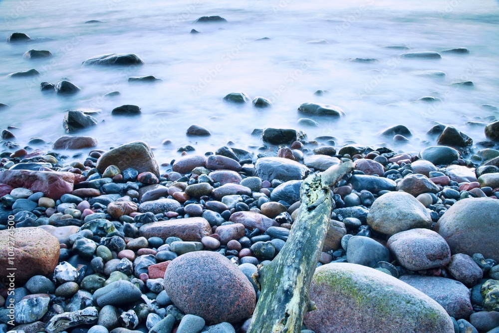 Obraz premium Romantic atmosphere in peaceful morning at sea. Big boulders sticking out from smooth wavy sea. Pink horizon