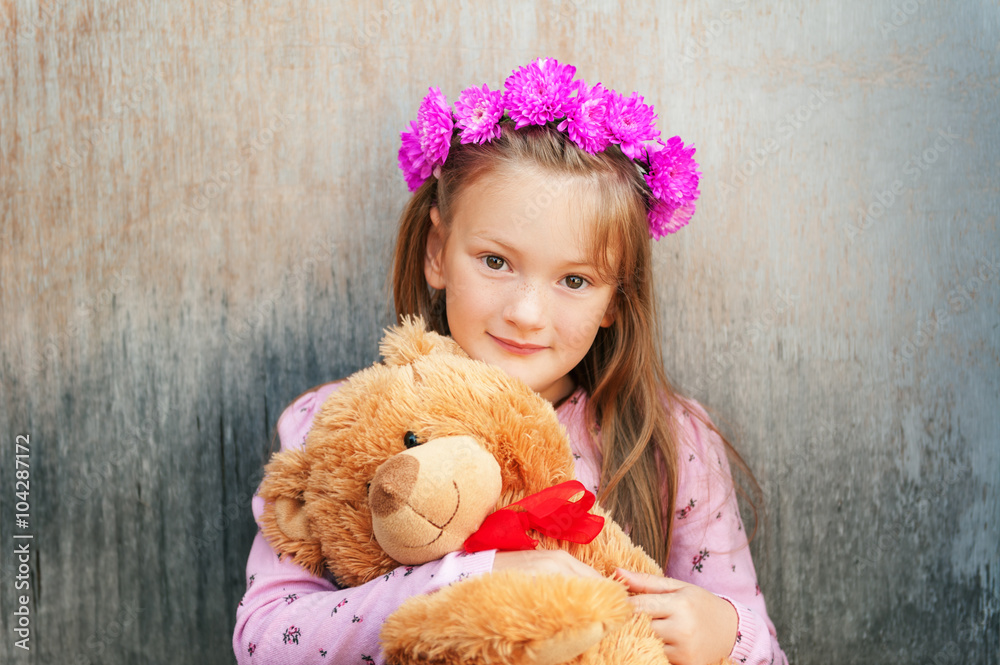 Close up portrait of adorable little girl with bright pink flower headband, holding teddy bear Close up portrait of adorable little girl with bright pink flower headband, holding teddy bear