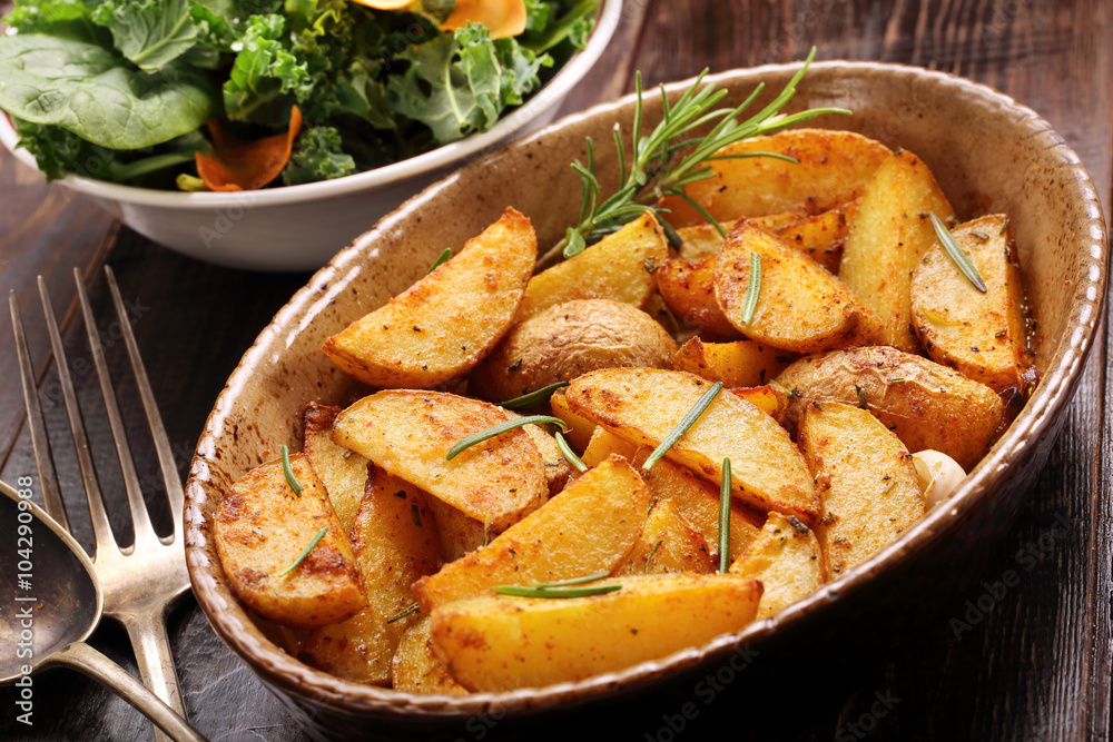 Roasted potato in brown bowl with fresh salad on wooden table Roasted potato in brown bowl with fresh salad on wooden table