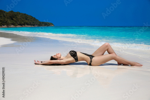 Beautiful sexy woman in black bikini lying on exotic tropical be