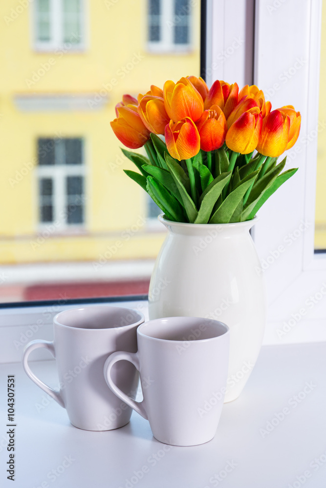 close up of beautiful orange flowers and two cups on a window si