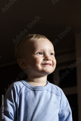 cute blonde boy looking towards the light happily smiling black background