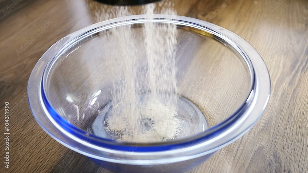 Close up of a fine curtain of refined white cake flour falling through a metal sievem, slow motion Close up of a fine curtain of refined white cake flour falling through a metal sievem, slow motion
