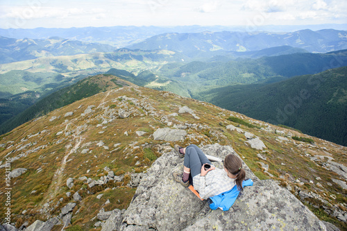 young girl sitting on a rock and drinking tea and admires beautiful landscape on a mountain top photo