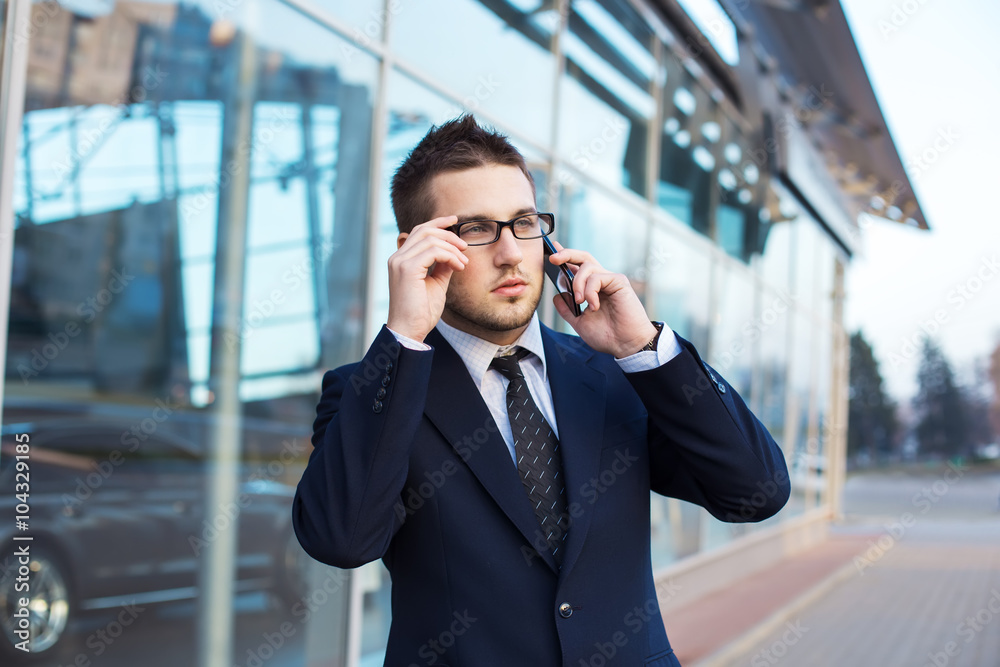 Attractive young businessman speak a cell phone, smiling. Standing in front of a modern office building. Attractive young businessman speak a cell phone, smiling. Standing in front of a modern office building.