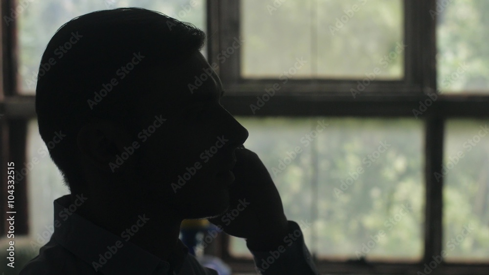 Silhouette of young man head answer the phone call. Indoor. Window on background