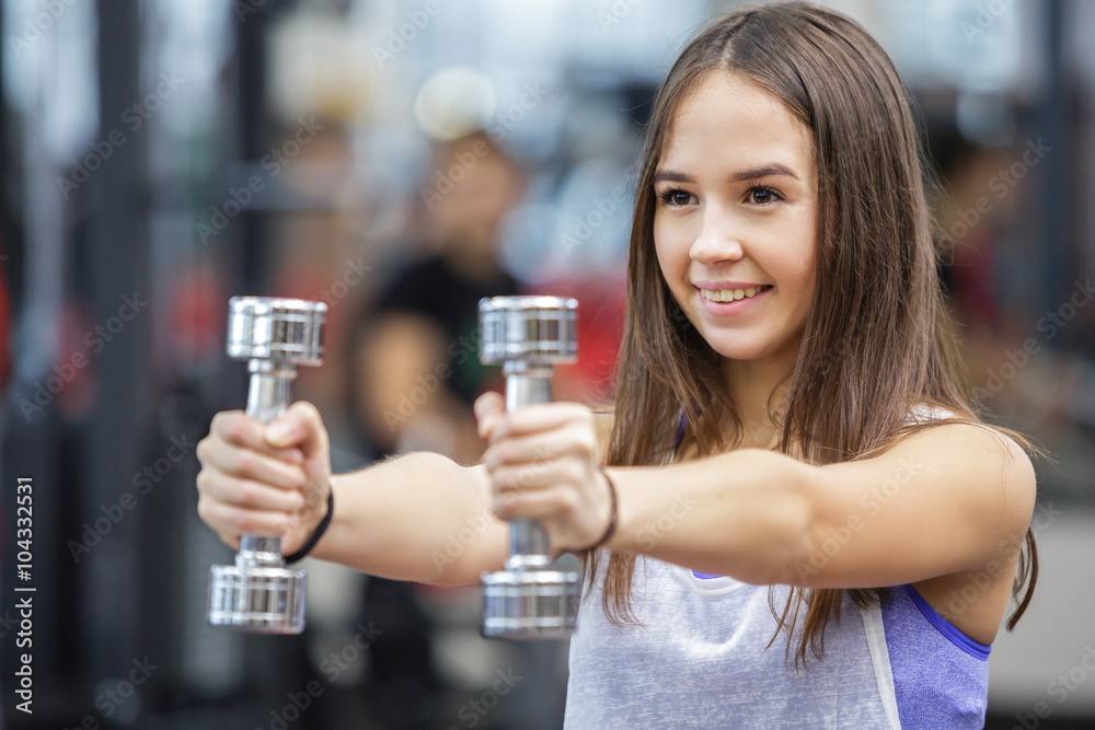 Young woman working out with two dumbbells in a gym Young woman working out with two dumbbells in a gym