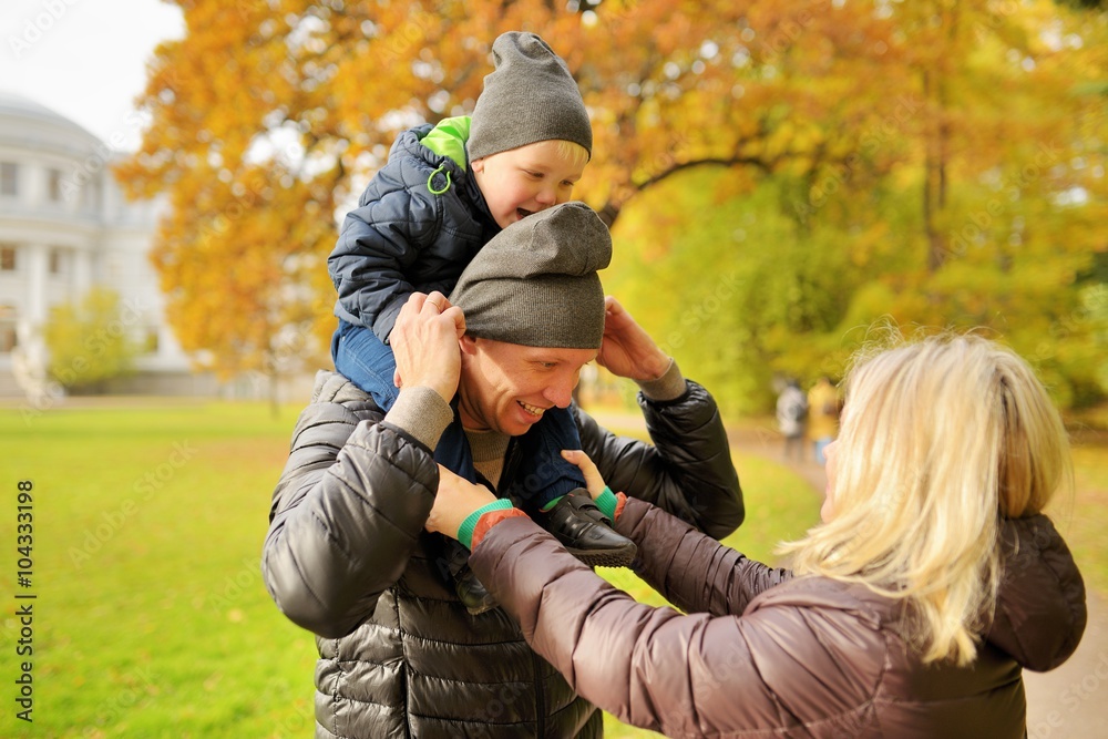 Wife corrects clothes for husband with child on a shoulders in park