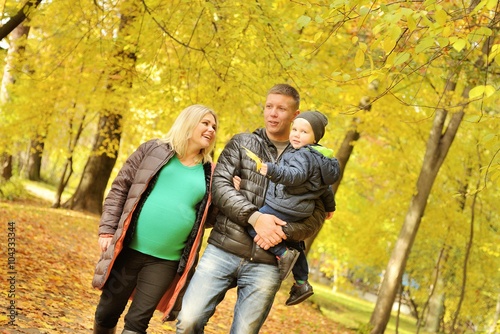 Pregnant young woman walking in autumn park with her husband and child