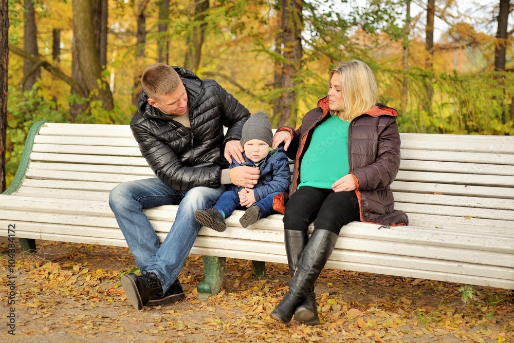 Family sits in autumn park on bench