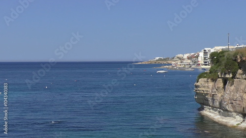 Man or woman in wetsuit swimming snorkeling snorkelling along coast of St Paul's Bay near Buggiba in Malta.At the end of coastline white round building of national aquarium.Suits as establishing shot photo