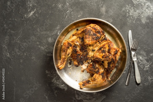 Obraz na plátně Chicken tabaka, Flattened and grilled on charcoal, Flattened Chicken - on a metal tray and black board table, with copy space