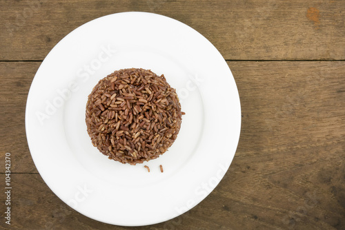 The cooked dark brown rice on the white plate on old wooden planks for good healthy.
