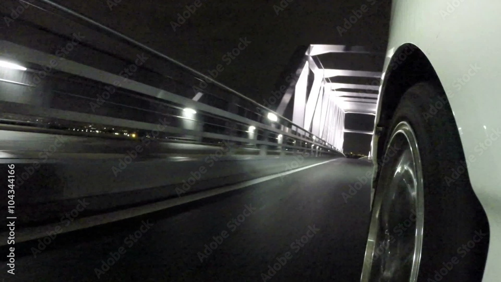 Front wheel variation of a car running through the nightscape of Tokyo's Gate Bridge.