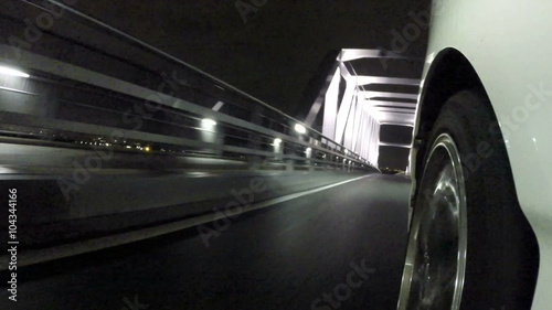 Front wheel variation of a car running through the nightscape of Tokyo's Gate Bridge.
