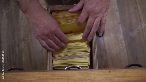 Overhead view shot of an anonymous man opening the drawer on a wooden card catalog and looking through the yellow index cards inside.