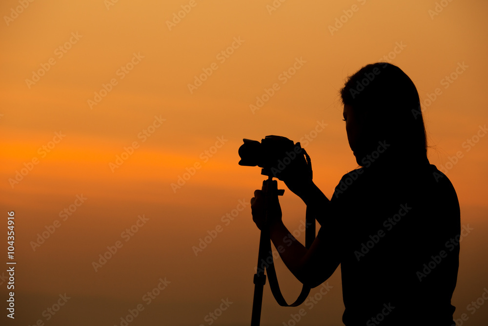 Silhouette of woman shooting with camera at sunset