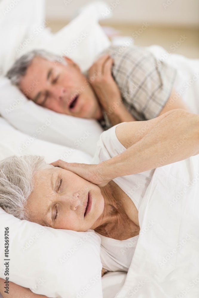 Awake senior woman in bed covering her ears Awake senior woman in bed covering her ears