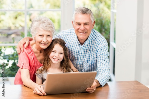 Portrait of smiling grandparents and granddaughter using laptop