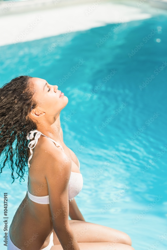 Beautiful woman in white bikini sitting by pool side