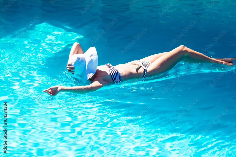 Woman wearing bikini and hat lying on air bed in pool