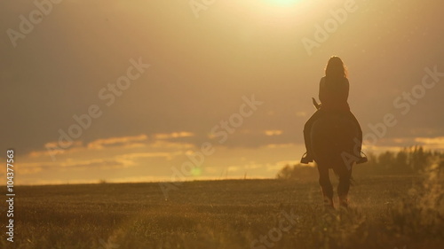 Young woman riding horse into bright sunset. Beautiful Young woman riding horse into amazing sunset