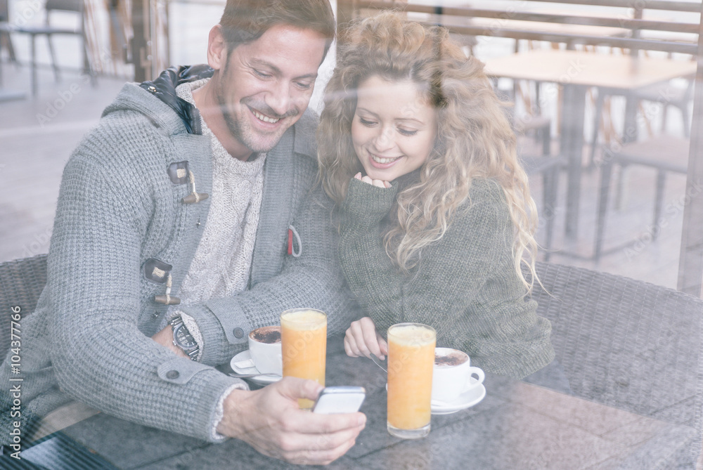 Happy couple sitting in a coffee shop looking at smartphone Happy couple sitting in a coffee shop looking at smartphone