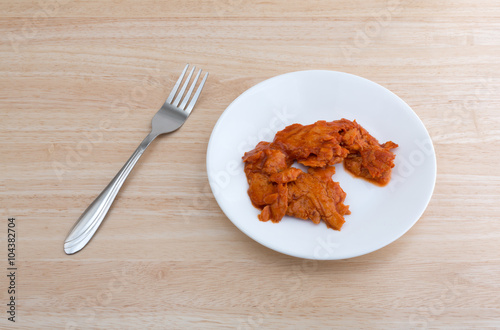 Spicy flavored pink salmon on a white plate with a fork to the side atop a wood table top.