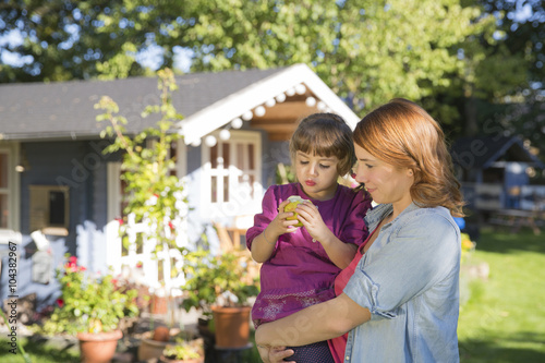 Mother holding daughter with apple in garden photo