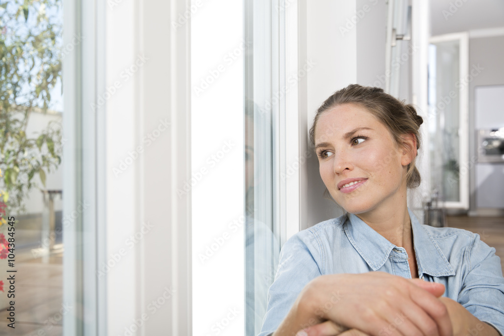 Young woman sitting at the window, hugging knees Young woman sitting at the window, hugging knees