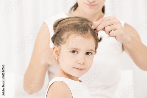 Portrait of expressive beautiful little girl smiling looking at the camera while her mother arranges her hair
