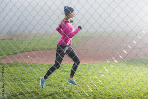 Young woman jogging on a meadow behind mesh wire fence