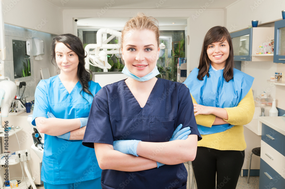 Obraz premium Dentist with crossed arms with patient and assistant behind her