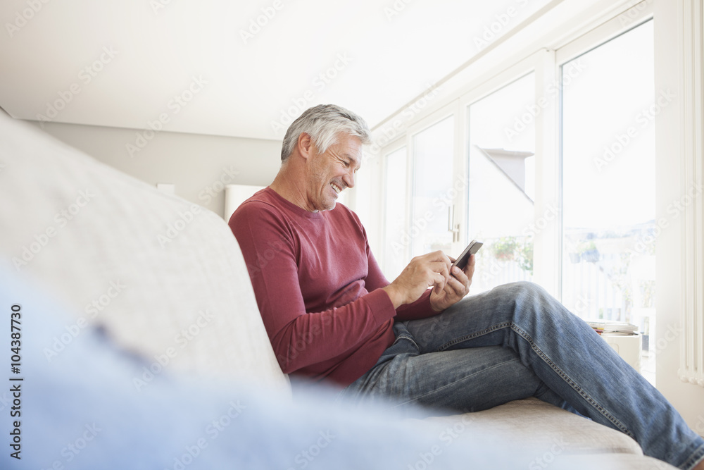 Smiling man sitting on the couch at home using smartphone Smiling man sitting on the couch at home using smartphone