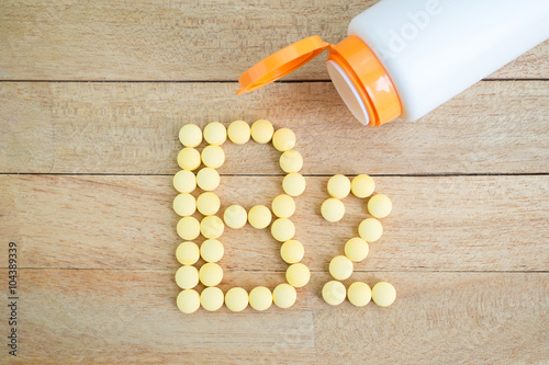 Photography Yellow pills forming shape to B2 alphabet on wood background