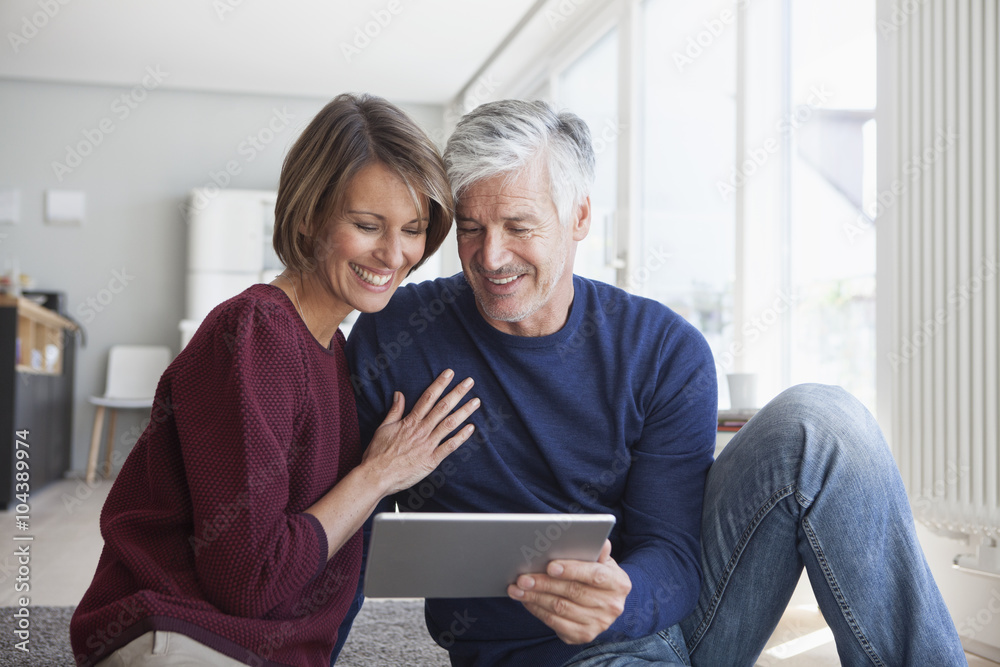 Smiling couple sitting on the floor at home looking at digital tablet Smiling couple sitting on the floor at home looking at digital tablet