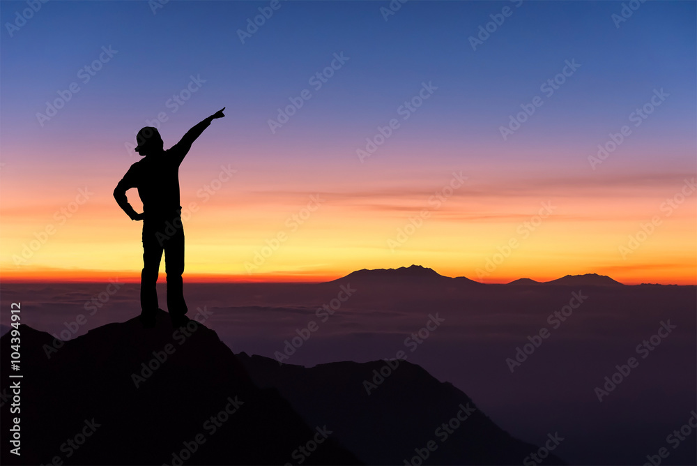 Silhouette of woman standing on the top of mountain and pointing to the sky